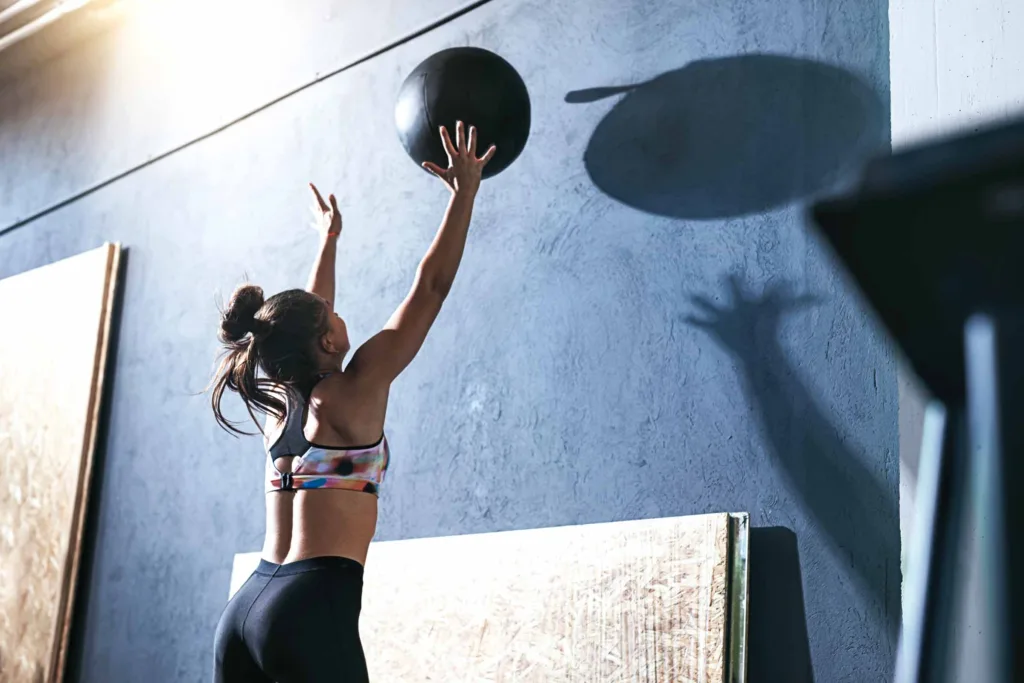 Athletic young woman athlete at the gym using a medicine ball for the wall ball exercises